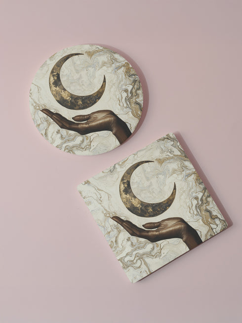 A ceramic coaster featuring a bronze-colored hand reaching toward an antiqued gold crescent moon against a swirling ivory and gold marble background, available in round and square shapes with cork backing.